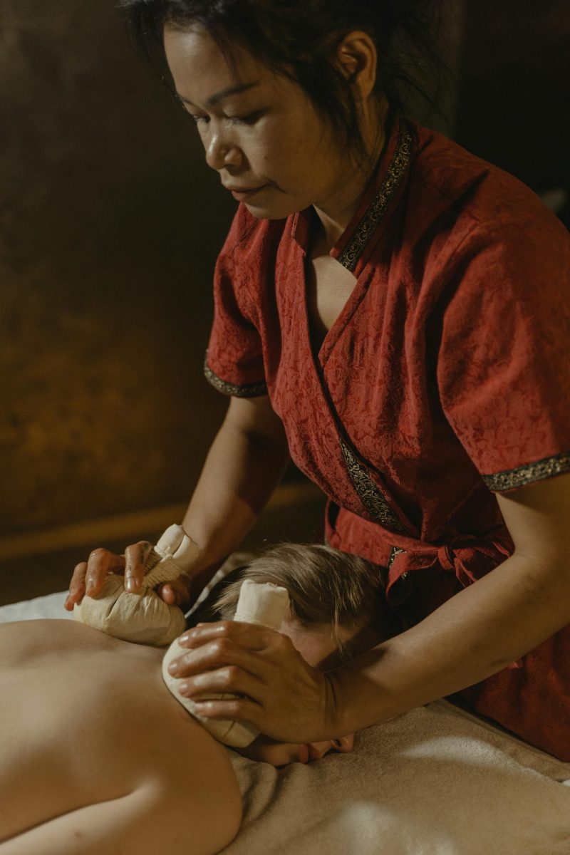 Asian masseuse using herbal compress for relaxing body massage in spa setting, promoting wellness.