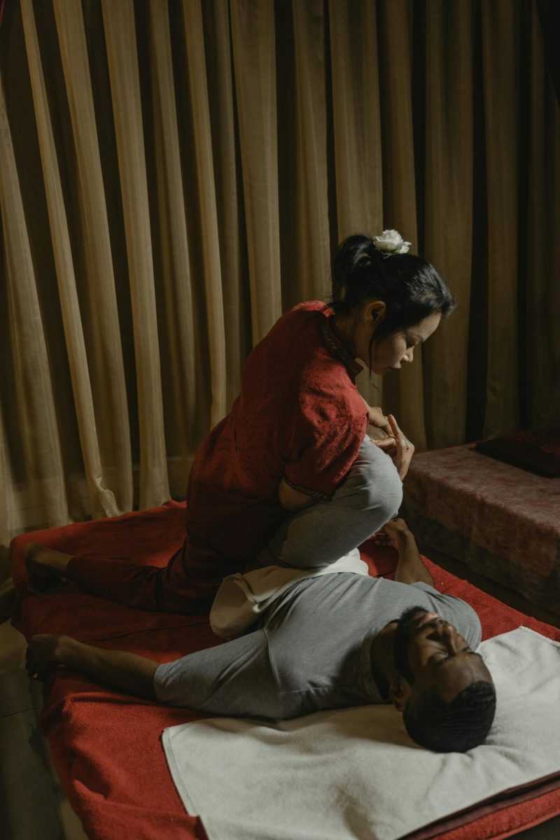 A therapist performs a massage in a dimly lit room, ensuring client relaxation and care.